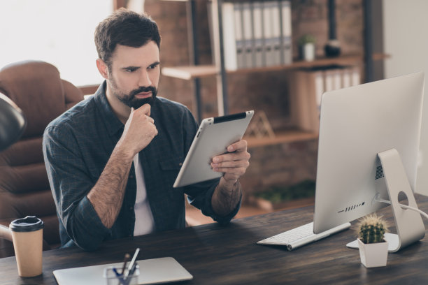 年轻专家在办公室桌子旁坐着，使用平板电脑的照片肖像图片下载