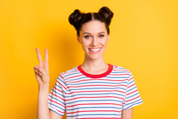 穿着条纹T恤的迷人年轻女孩在黄色背景下做出V字手势的照片图片下载