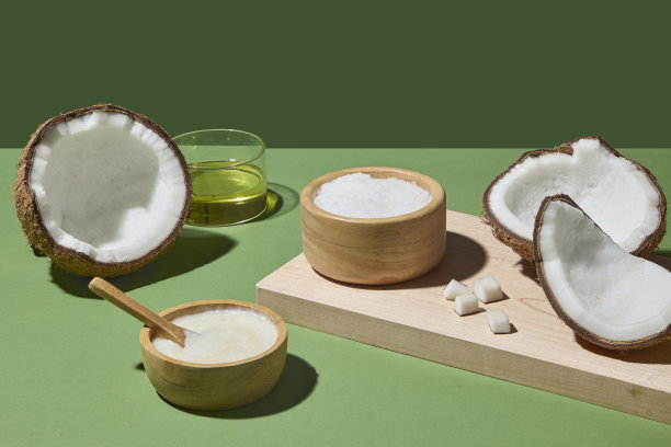 椰子、油和木碗精心排列。这张照片强调了椰子在护发油、身体磨砂和水疗灵感产品中的多功能性，背景为绿色。图片下载