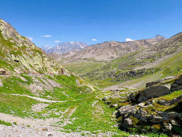 从圣伯纳德山口的山顶俯瞰，瑞士一侧展现出令人叹为观止的阿尔卑斯山谷、崎岖的山峰和蜿蜒的山路，映衬在晴朗、阳光明媚的夏日天空下。图片下载