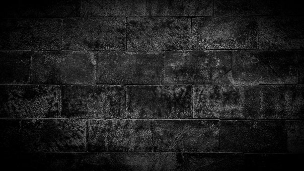 黑色石砖墙的特写照片，呈矩形块状图案。粗糙的纹理表面赋予其乡村、坚固和复古的外观。适合用作背景、壁纸或设计元素。图片下载