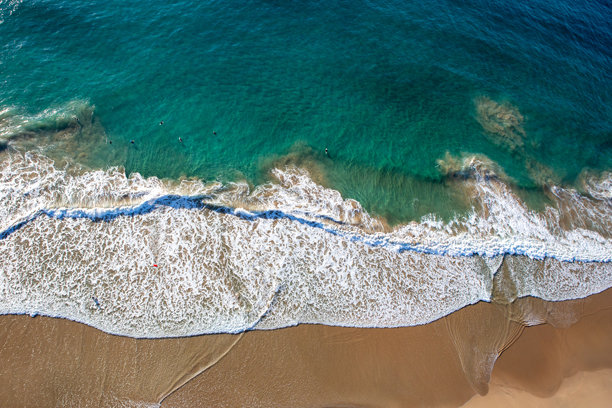 各种冲浪者漂浮在碧绿色的海岸浪潮中，沙滩上波浪拍打着沙子。照片从新南威尔士州南海岸的高空拍摄。图片下载