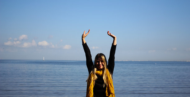 穿着毛衣和围巾的女人在海边双臂高举，洋溢着快乐。自然生活方式的照片捕捉了秋季宁静的散步和海岸边的日常幸福。图片下载