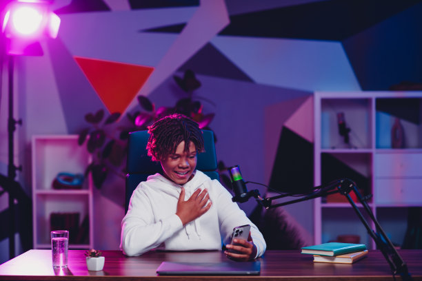 年轻的博主穿着时尚的连帽衫，在现代工作空间中与观众通过智能手机互动，周围环绕着明亮的霓虹灯。图片下载