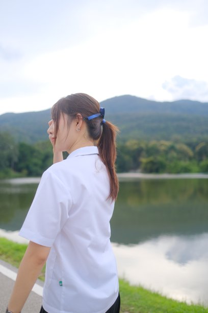 一位穿着白衬衫、扎着蓝色发带的女性正站在湖边。学生女孩的概念。图片下载