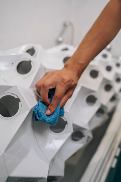 垂直裁剪的照片，男人用蓝色布擦拭白色水培系统，维护室内植物茁壮成长的洁净环境。图片下载