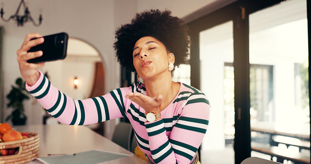 女性在家中吹吻或自拍，适用于社交媒体、更新博客或在线互动。非洲影响者在家中拍摄照片或做手势，以便在约会应用中互动、吸引粉丝或建立联系。图片下载