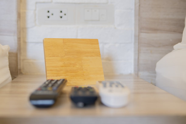 酒店卧室内木质床头柜上放着空的木板，旁边有电视遥控器。图片下载