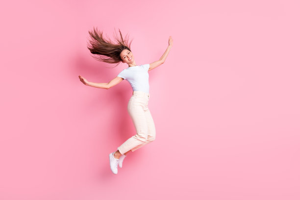 乐观的棕发女士穿着T恤和裤子在粉色背景上跳跃的全身侧面照片图片下载