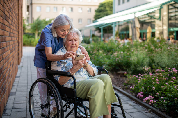 坐在轮椅上的老年患者向护理人员展示智能手机中的图片。图片下载