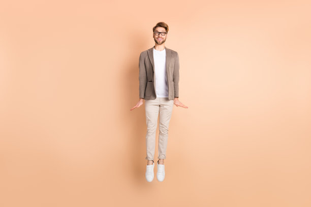 充满活力的年轻男子在米色背景上跳起，心情愉快的全身照片图片下载