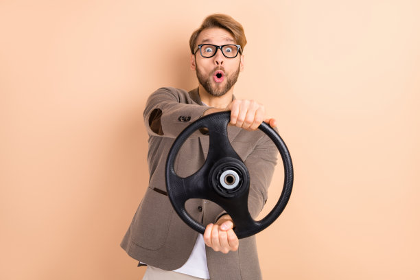 戴眼镜的震惊、惊讶的商人在米色背景下快速驾驶汽车的照片图片下载