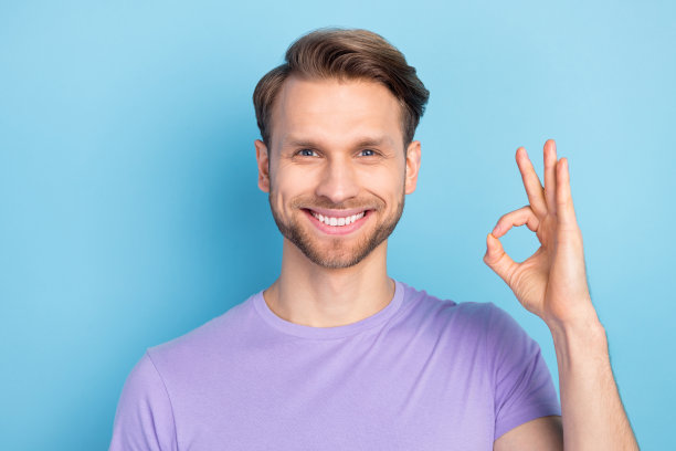 穿着紫色衣服的男人在淡蓝色背景下微笑并做出“好”的手势的照片肖像图片下载