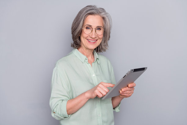 快乐、微笑、开朗、可爱的年轻女商人在灰色背景下戴着眼镜使用平板电脑的照片图片下载