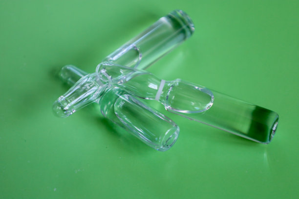 一组不同大小的透明玻璃安瓿瓶横放在坚实的绿色背景上。这张照片展示了药品、实验室研究和医疗设备，象征着治疗和科学。图片下载