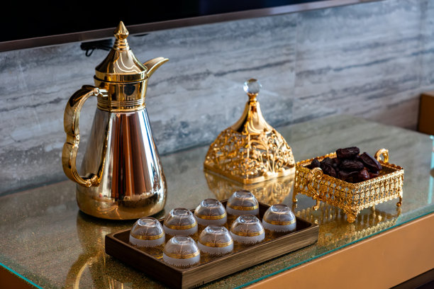 照片中，一只金色的阿拉伯咖啡壶放在桌子上，旁边有枣子和杯子。这是一个典型的传统场景，常见于卡塔尔、阿联酋和沙特阿拉伯等富裕的中东国家。图片下载