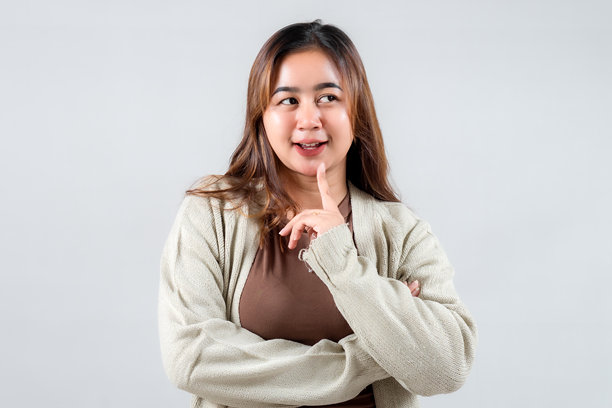 一位顽皮的年轻女性用手指轻触嘴唇，暗示着秘密。她的休闲装扮和富有表现力的神态使这张图片非常适合生活方式、社交媒体和创意项目。图片下载