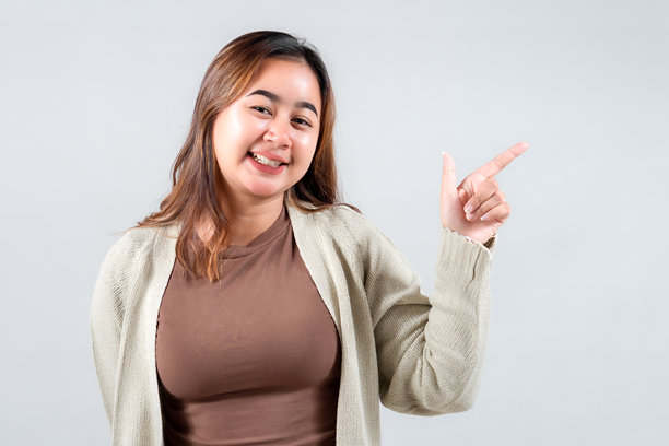 一位面带灿烂笑容的年轻女性微笑着指向一侧，展现出她的休闲风格。这张引人入胜的图片非常适合用于传达积极情绪的生活方式、社交媒体和创意项目。图片下载