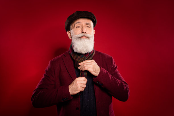 祖父穿着围巾、夹克和帽子的照片肖像，准备参加会议，背景为鲜艳的红色。图片下载