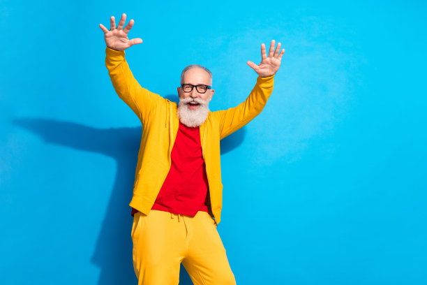 穿着黄色运动服的古怪快乐兴奋的祖父在蓝色背景下跳舞的照片图片下载