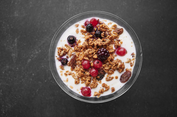 一杯新鲜酸奶，上面放有谷物和水果，背景为灰色。图片下载