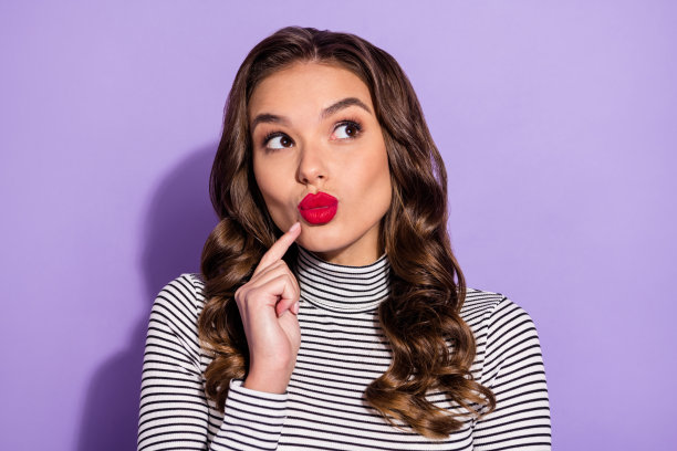穿着条纹服装、指着手指、撅嘴的闪亮年轻女性照片，背景为紫色。图片下载