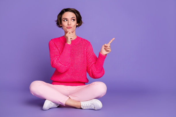 年轻女孩坐在地板上，手托着下巴思考，手指指向空白区域，背景为紫色，适合广告宣传的全身照片。图片下载