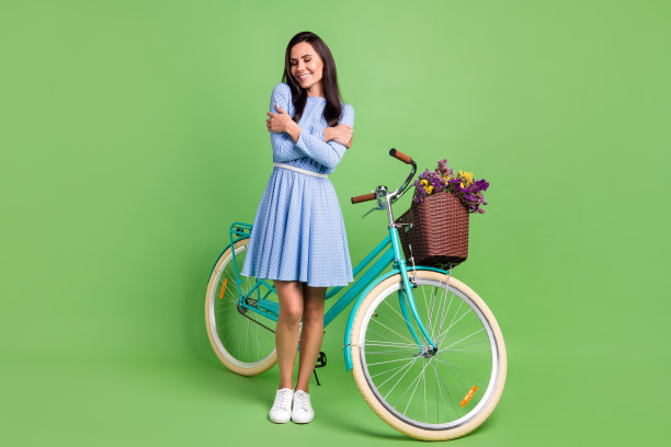 乐观的棕发女士穿着骑行服装，双手抱住自己，站在绿色背景前的全身照片图片下载