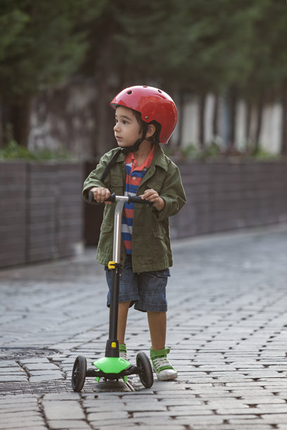 学龄前男孩在鹅卵石街道上骑滑板车的照片。图片下载