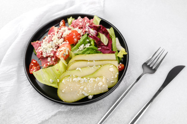 健康沙拉，搭配梨和奶酪，放在黑色碗中，背景为白色，适合清淡饮食或食谱内容图片下载