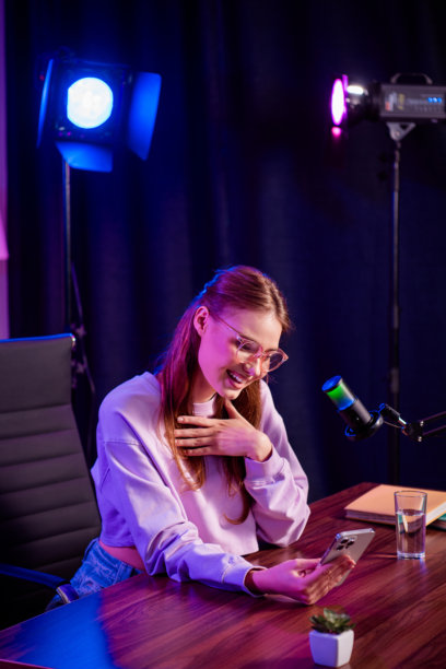 年轻女性博主戴着眼镜，在时尚的桌面设置中，配有霓虹灯和麦克风进行直播图片下载