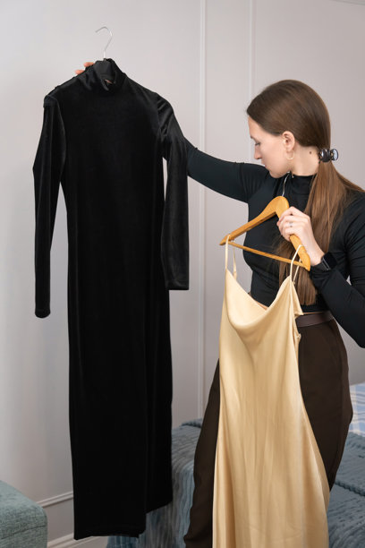 专业时装设计师手持两件衣服在比较，一件黑色天鹅绒裙子和一件金色丝绸裙子，同时决定哪一件更适合她的新系列。竖版照片图片下载