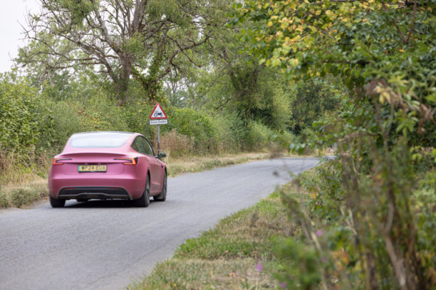 环保的特斯拉汽车在英国科茨沃尔德的西伦斯特附近一条偏远的小县道上行驶。图片下载