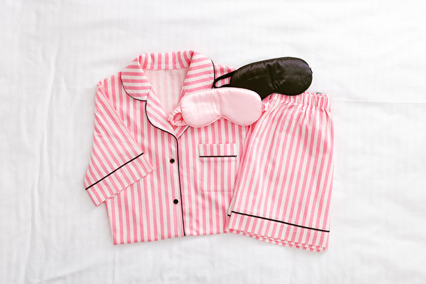 从上方俯视折叠的鲜艳粉色女性睡衣，搭配黑色和粉色的缎面睡眠眼罩，放在白色床上。明亮的平铺舒适睡衣，适合睡眠和放松。时尚睡衣的美学生活方式照片。图片下载