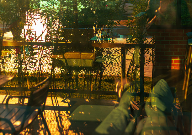 早晨阳光照射在咖啡店内部玻璃上的景象，模糊的背景是阳光洒落的咖啡店内部，桌子、椅子和玻璃罐中的花卉布置在黄昏时分。模糊背景照片。图片下载