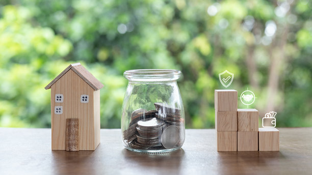木屋模型旁边放着一个装满硬币的玻璃罐和堆叠的积木，展示了金融图标。房地产投资、抵押贷款、储蓄理财和长期物业商业增长的概念。图片下载
