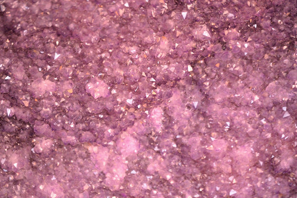 一幅生动的全画幅微距照片，展示了一个充满闪耀紫水晶的晶洞。水晶的大小和透明度各不相同，形成了迷人的紫色和粉色纹理，捕捉光线，呈现出闪闪发光的效果。图片下载