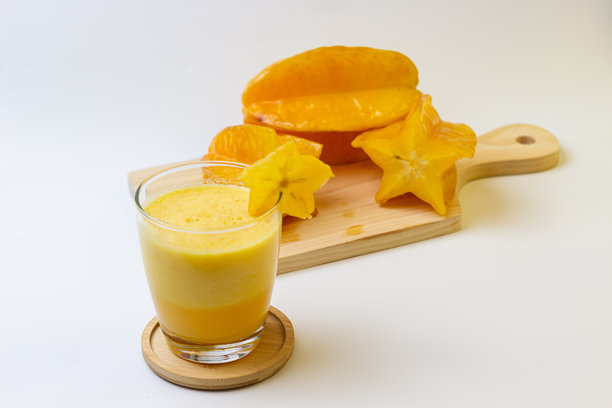 明亮的黄色冰沙，搭配新鲜的杨桃，放在木板上的玻璃杯中，简约干净的照片。图片下载