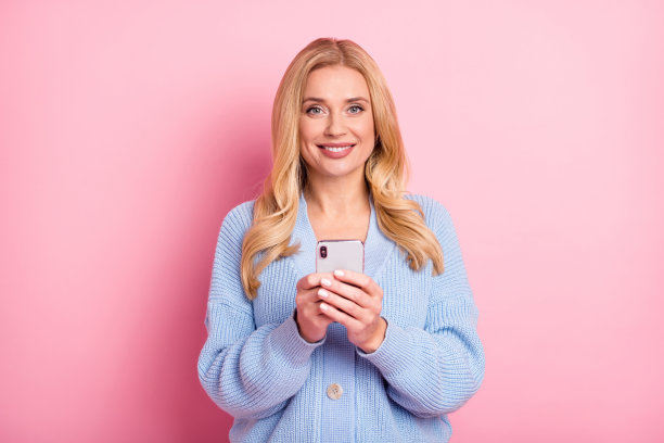 使用手机浏览互联网的波浪卷发女性照片肖像，背景为柔和的粉色。图片下载