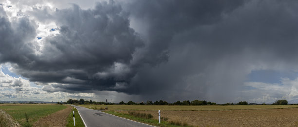 一幅全景照片，展示了暴风雨横扫全国，伴随着大雨和戏剧性的云层形成，前景是一个农业田野。图片下载