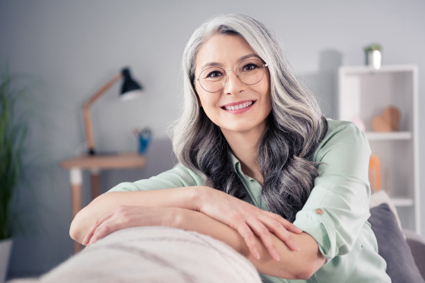 戴眼镜的银发老年女性微笑着坐在沙发上的人像照片图片下载