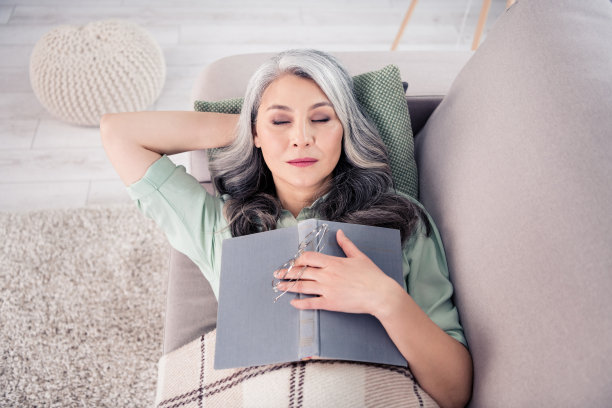 老年女性躺在沙发上睡觉，手中握着书和眼镜的俯视照片图片下载