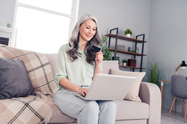 老年女性坐在房间里，使用电脑在线购物并用信用卡付款的照片肖像图片下载