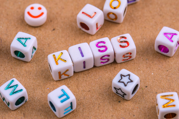 字母珠子拼写的“KISS”中央排列在一个有纹理的表面上。图片下载