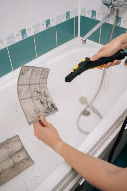 专业暖通空调技术人员在浴室中使用吸尘器清洁脏空调滤网，进行维护的竖直裁剪照片图片下载