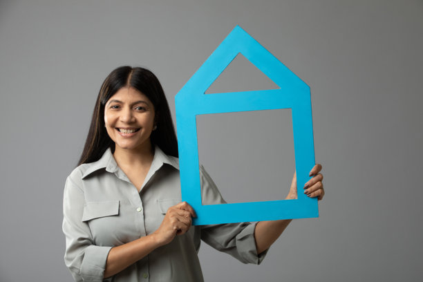 一位快乐的女性手持并展示木制房屋模型的照片。图片下载