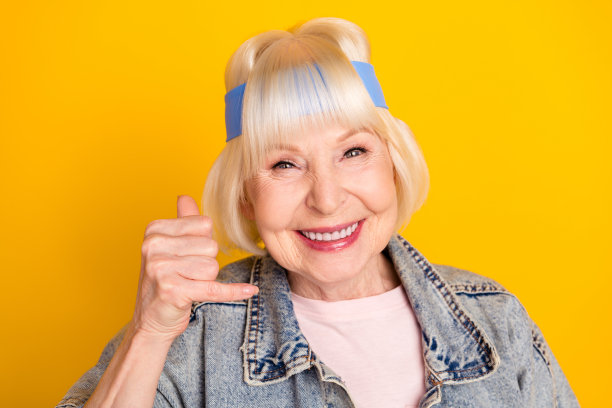 微笑的老年女性在明亮的黄色背景上做出“给我打电话”的手势肖像照片图片下载