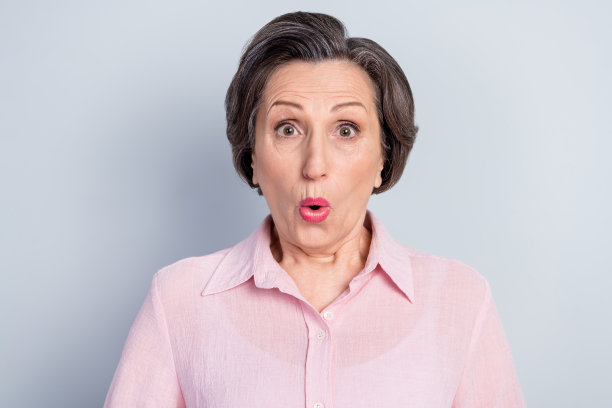 穿着粉色衣服、眼睛大大的、嘴唇撅起的惊讶搞笑年轻女士的照片，背景为灰色。图片下载