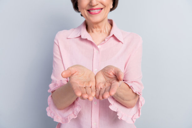 一位穿着粉色衣服的年轻女士，微笑着双臂张开，站在灰色背景前，照片经过裁剪，显得宁静而光亮。图片下载