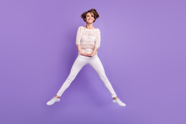 可爱的年轻女士穿着白衬衫在紫色背景下高高跳起的全身照片图片下载